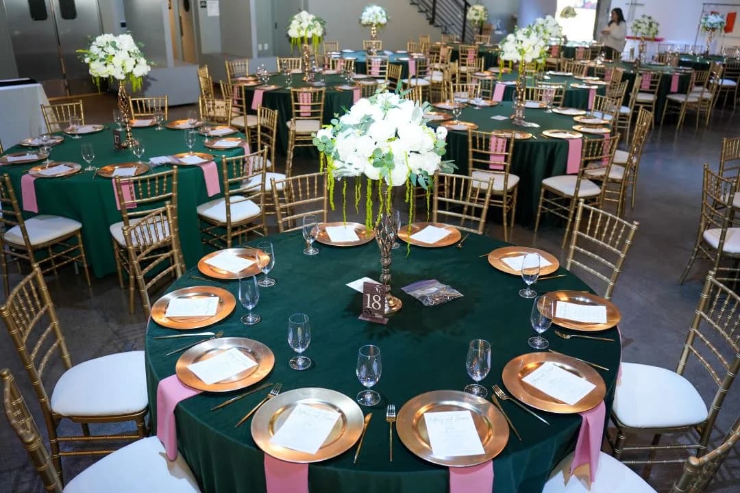 Banquet room of round tables in emerald linen with gold chairs, rose-gold chargers and tall white centerpieces
